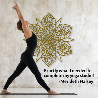 Woman in black yoga attire performing a pose with a decorative gold mandala on a textured wall.