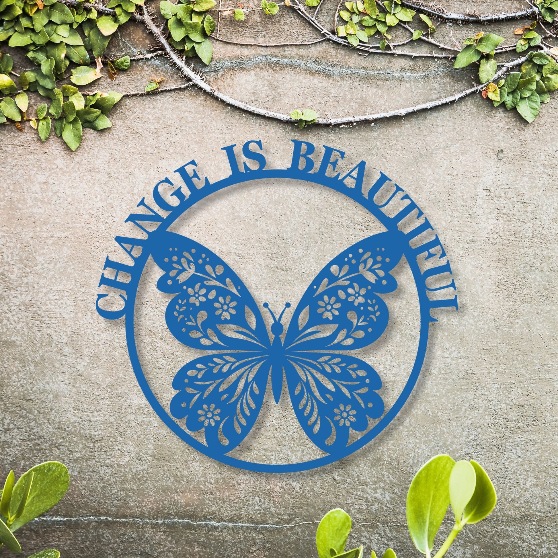 Blue butterfly-shaped metal sign with 'Change is Beautiful' text on a stone surface with greenery.