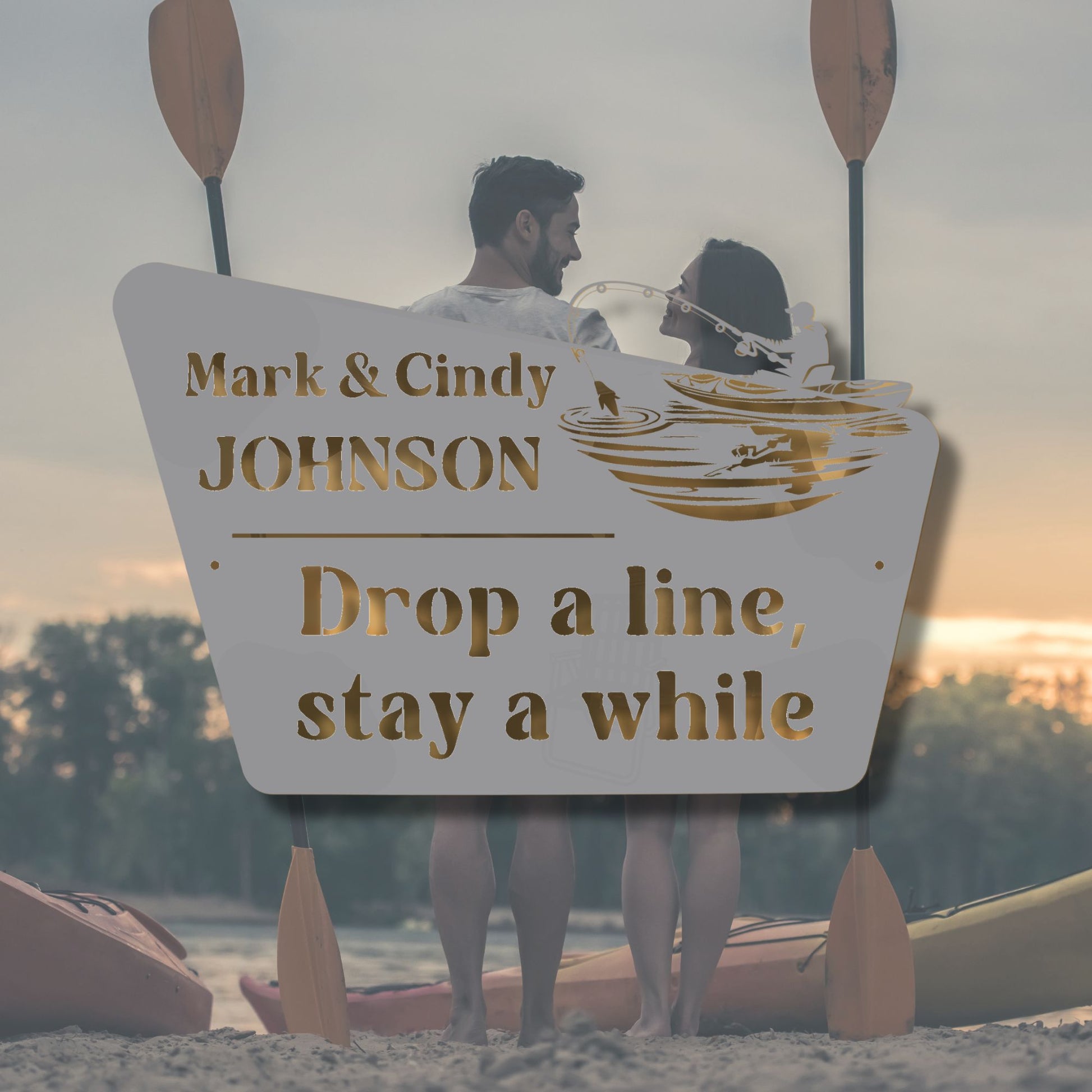 Two people in a kayak with a personalized sign behind them, set against a sunset.