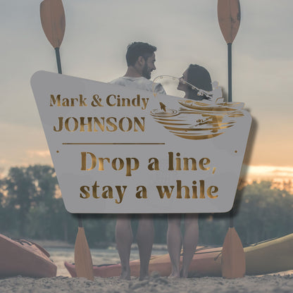 Two people in a kayak with a personalized sign behind them, set against a sunset.