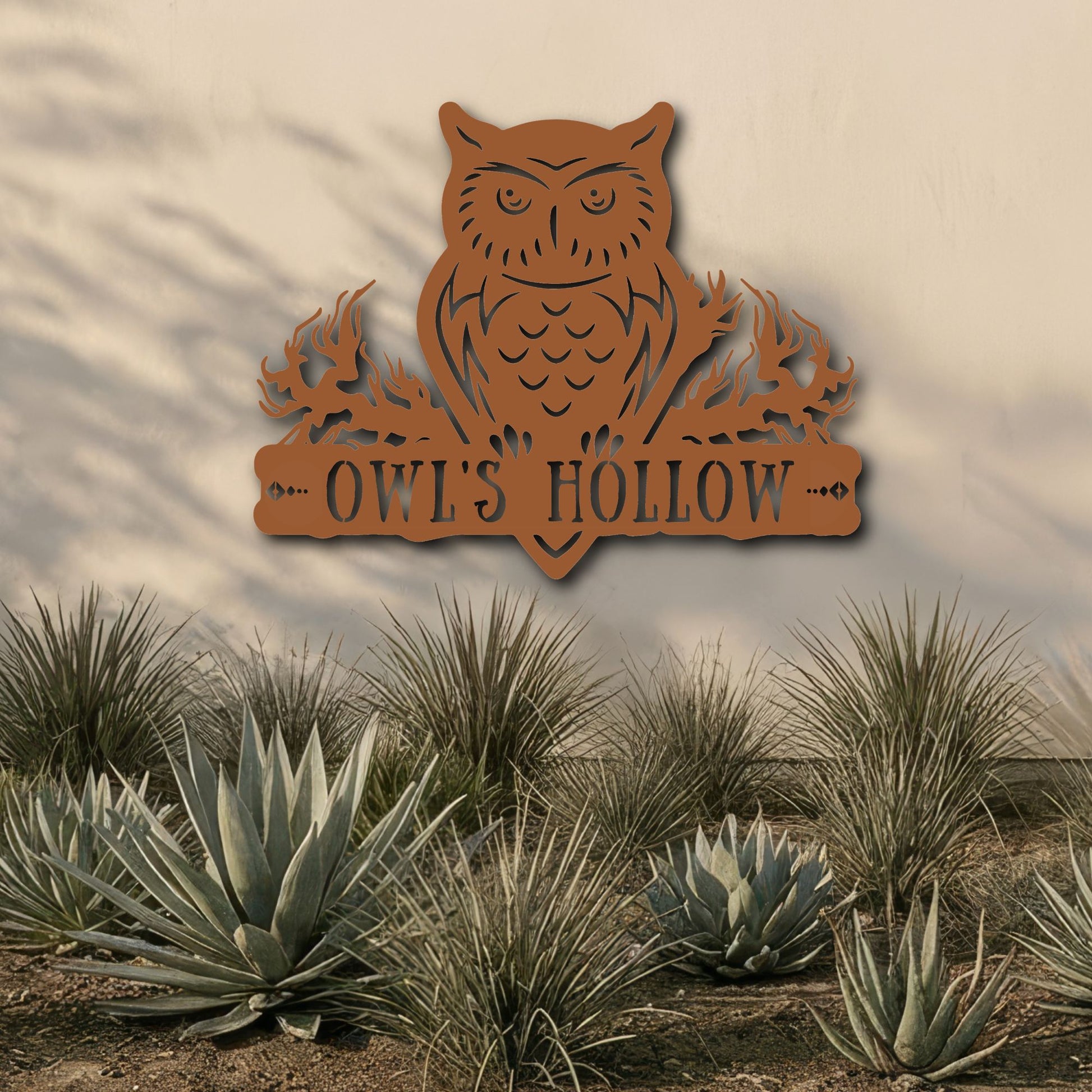 Decorative metal owl sign with 'OWL'S HOLLOW' text in a desert landscape.