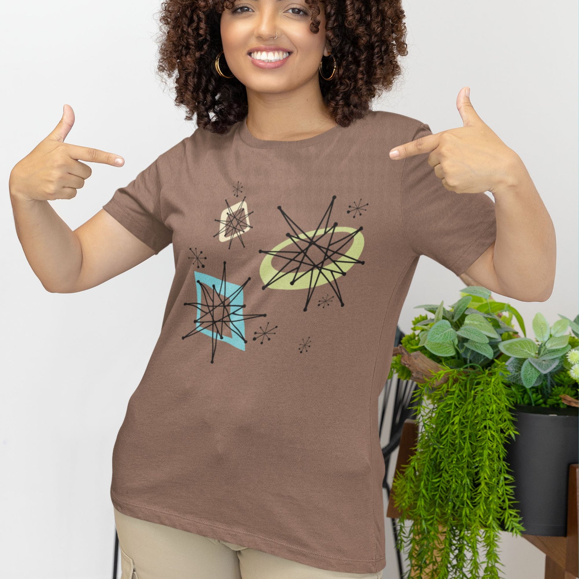 Woman wearing a brown t-shirt with abstract designs, pointing at the shirt.