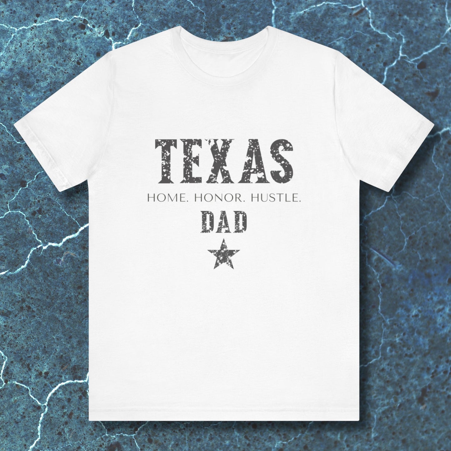 White t-shirt with 'TEXAS HOME HONOR HUSTLE DAD' text on a textured blue background
