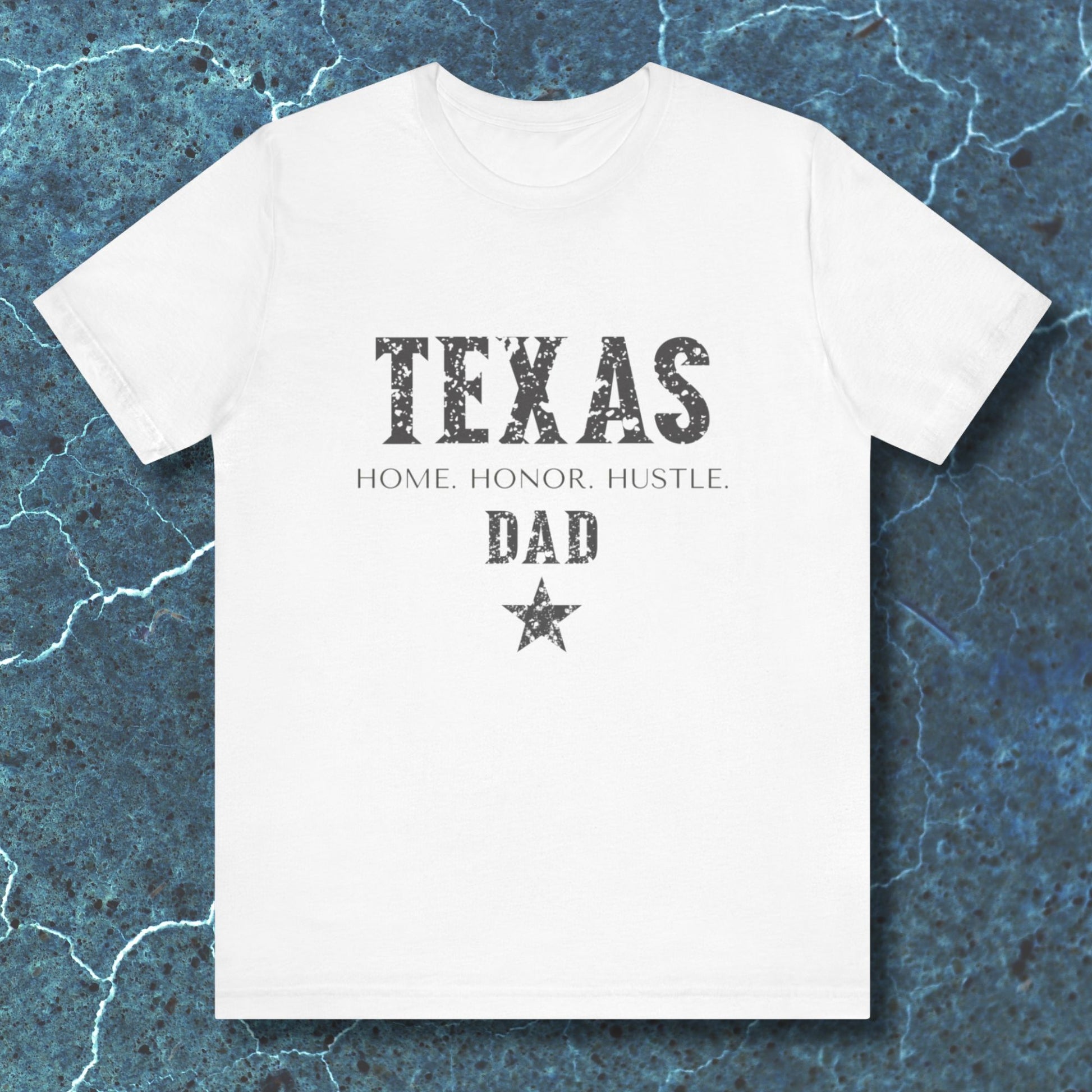 White t-shirt with 'TEXAS HOME HONOR HUSTLE DAD' text on a textured blue background