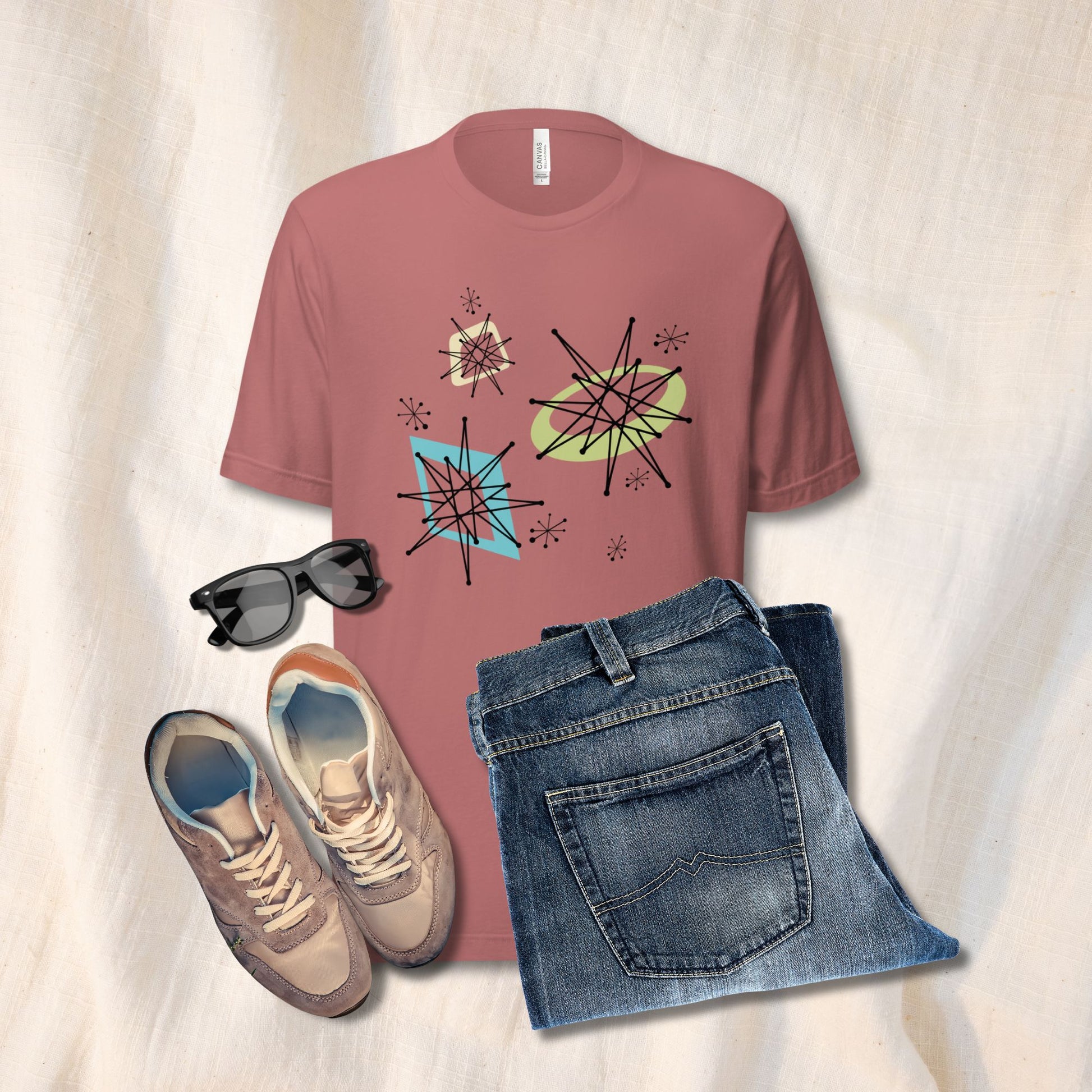 T-shirt with abstract design, sunglasses, sneakers, and jeans on a light background